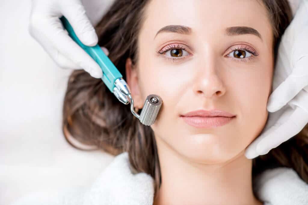 Portfolio 7 Young womens Face with - MICRONEEDLING FOR ACNE SCARS Cosmetologist holding Dermaroller and woman's face in hands | Glam Bar Medical Spa in Los Angeles CA